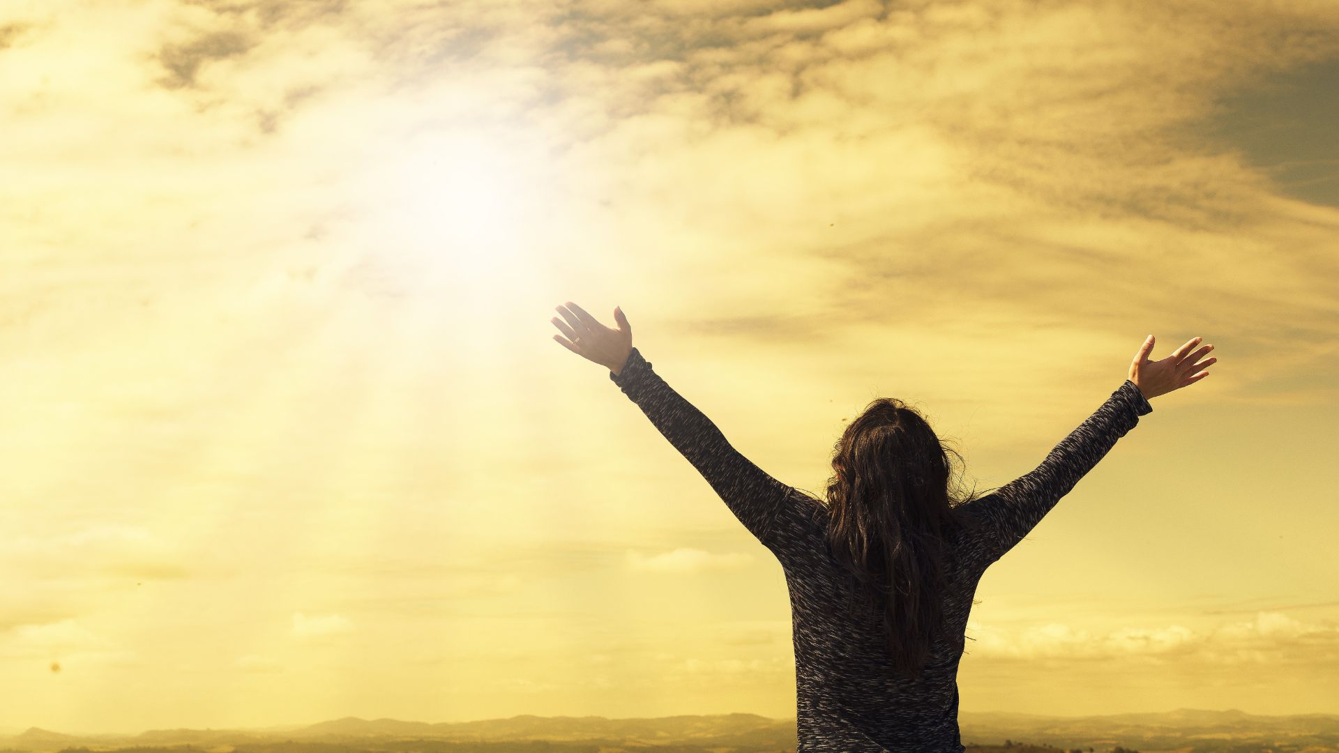 mulher adorando a Deus com as mãos para cima diante do sol