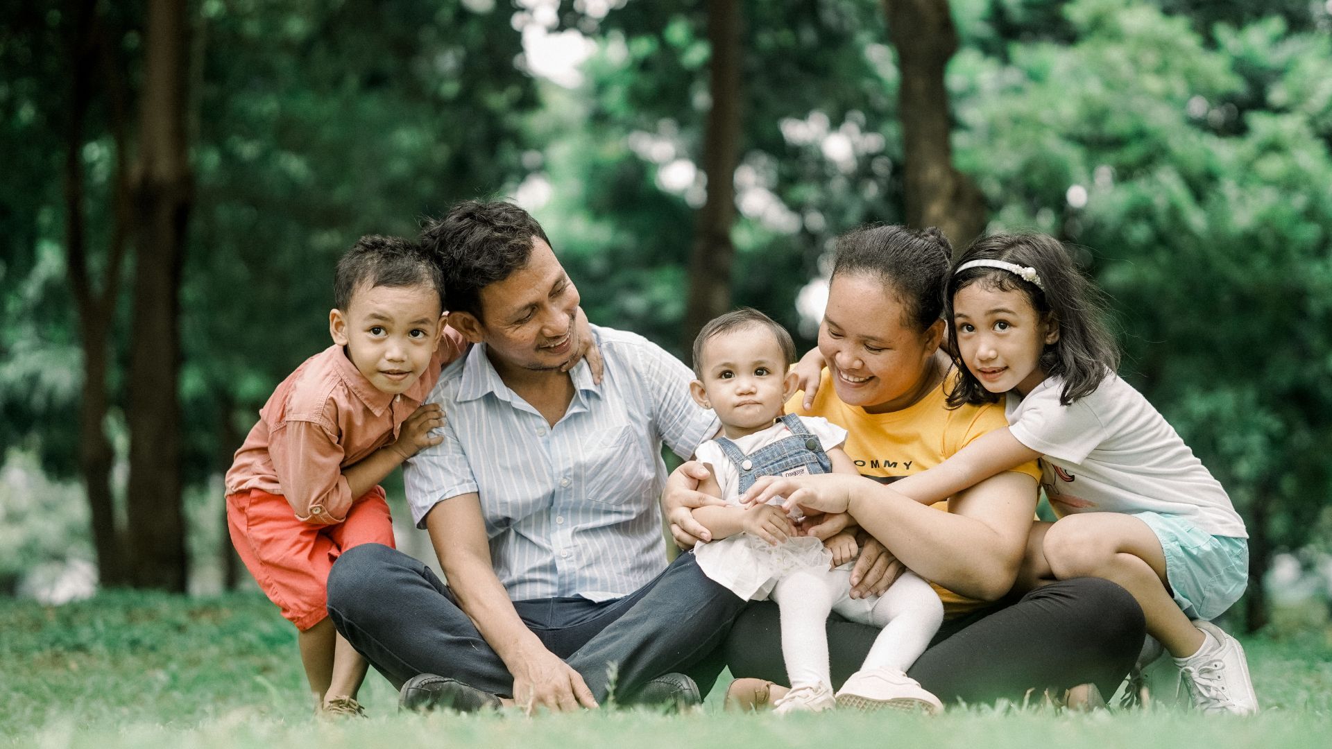 pai e mãe com com três filhos pequenos sentados na grama felizes