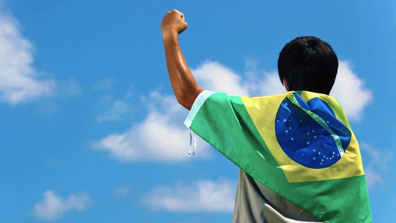 homem com a bandeira do Brasil nas costas comemorando